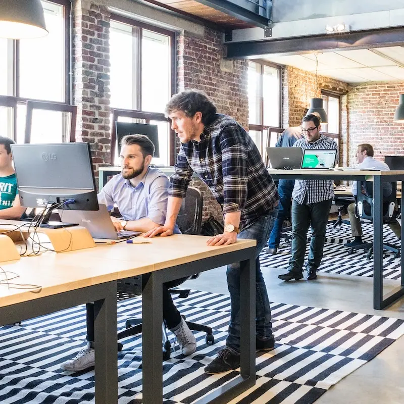 A man standing with fellow works in an office that looks like a startup.
